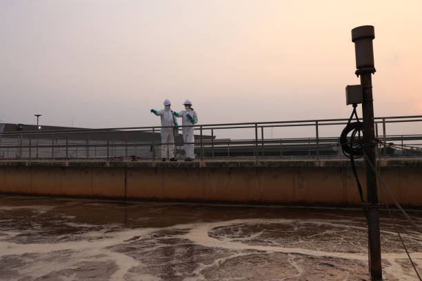 istock scientist and safety  engineer wearing chemical PPE protection work at wastewater treatment plant with tablets and survey patrol  on the  wastewater tanks 2154756841