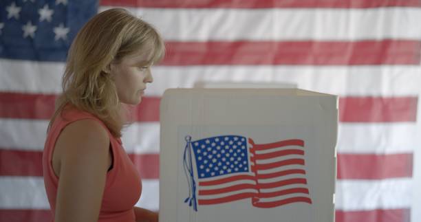 istock Profile MS young woman standing at voting booth, US flag behind 2154771517