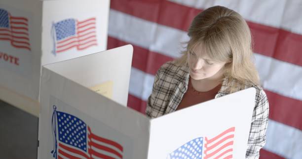 istock MS from high viewpoint, young woman votes in election, US flag behind 2154771528