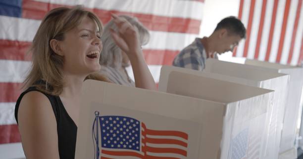istock Young woman laughs while voting in election, US flag behind 2154771530