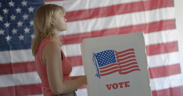 istock Angled MS young woman voting, considering candidates, US flag behind 2154771540
