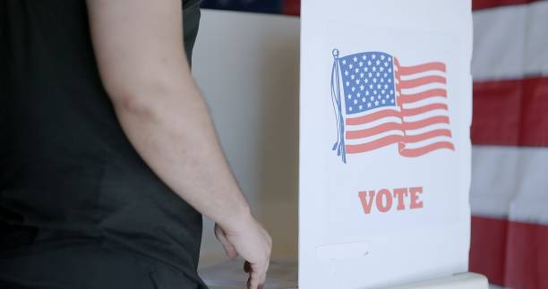 istock Close up from behind dark skinned voter casting ballot at US election booth 2154771584