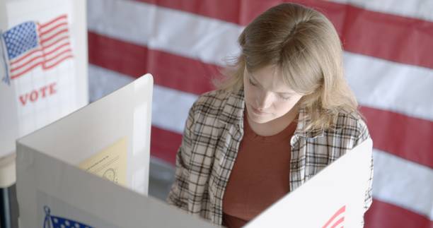 istock Medium shot, high view, young woman votes, US flag behind 2154771639
