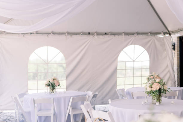 istock A tented backyard wedding reception with white tables and simple flower arrangement in the center of each table. 2154772974