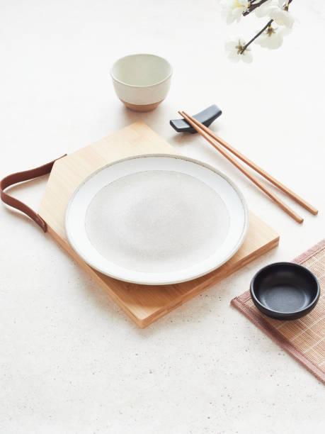 istock Simplicity in tableware, white and black minimalist oriental setting table. Plate on bamboo board, black bowl, chopsticks and bowl. Delicate flower on the table. 2154774740