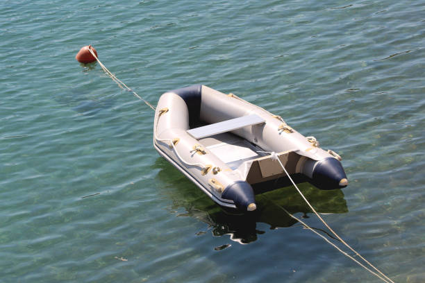 Small inflatable grey and dark blue rubber flatbeat dinghy boat with high quality reinforced aluminum floor tied to orange navigational buoy and anchored in local harbor surrounded with calm blue sea on warm sunny spring day