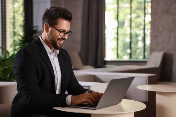 istock Happy young man with glasses working on laptop at table in office 2154786169