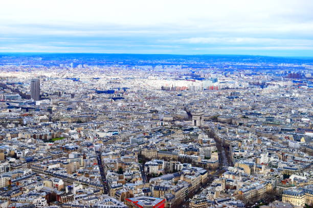An wide aerial view of the Arc de Triomphe showing the roads of Paris circling around the arch. Montparnasse Tower, sometimes referred to as the middle finger of Paris, can be seen on the left.