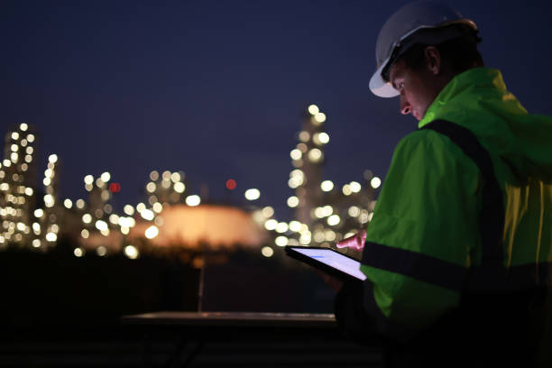 istock A night shift engineer in a hard hat and reflective jacket is focused on a tablet with the illuminated industrial plant in the background. 2154791413