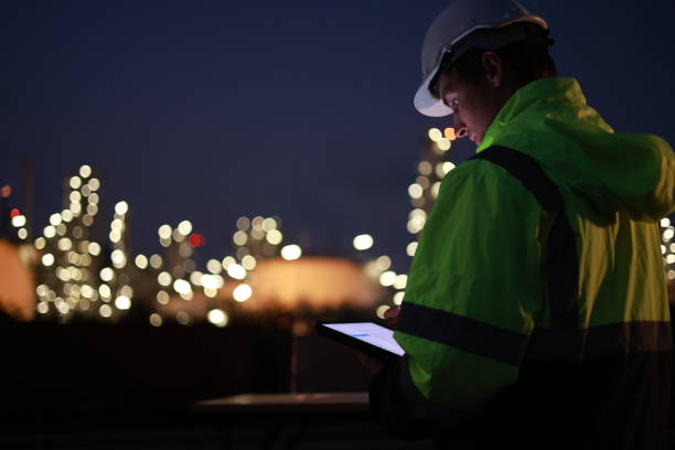 istock A night shift engineer in a hard hat and reflective jacket is focused on a tablet with the illuminated industrial plant in the background. 2154791415