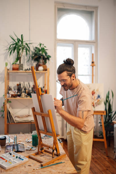 istock Tattooed hipster artist painting on easel at creative art studio. 2154795463