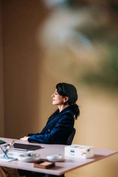 A professional woman sits thoughtfully at her desk in a modern office, exhibiting a sense of calm and contemplation amidst her business environment.