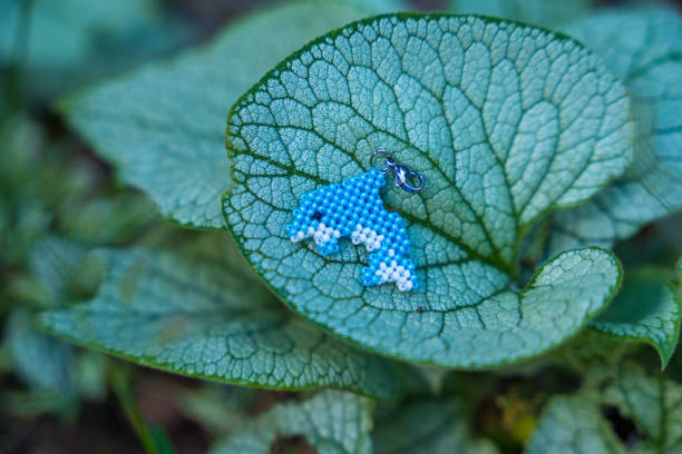 A beaded dolphin keychain is on a large live plant leaf in nature. Handcrafted concept.