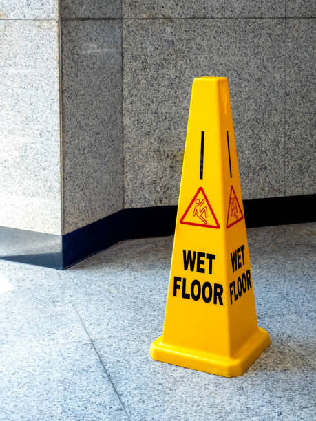 istock Wet floor caution sign on walkway in modern building. Warning red slip and fall people and text WET FLOOR, sign on yellow plastic rubber cone on granite floor with copy space, vertical style. 2154807341