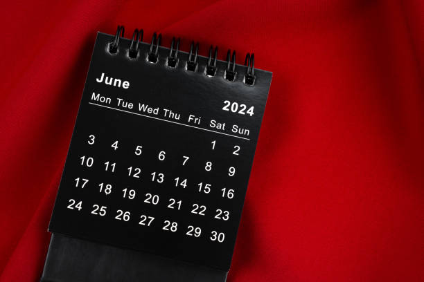 istock June 2024 Black spiral desktop calendar on red textile. 2154811638