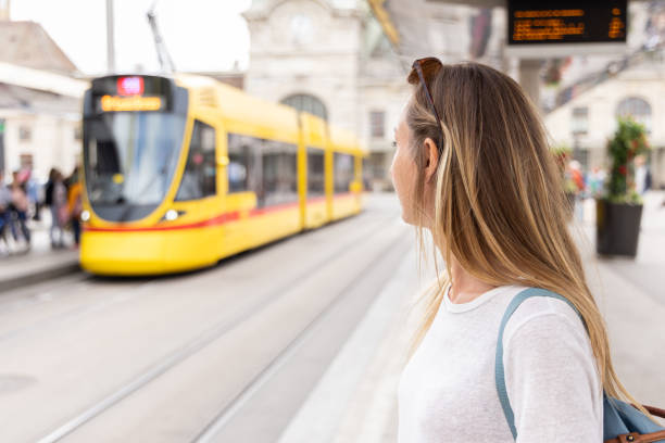 istock Woman Watching Yellow Tram Arrive at Station 2154824465
