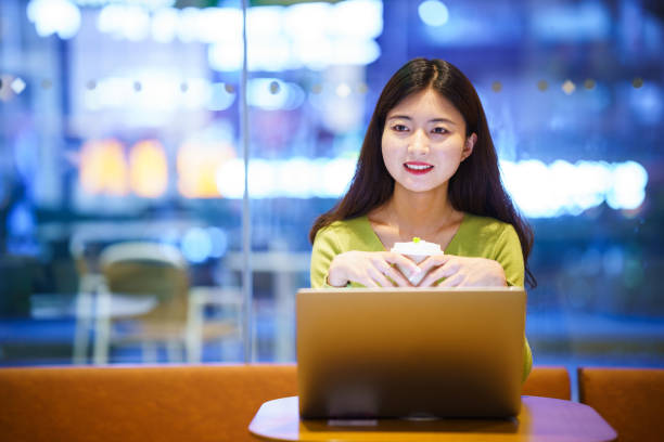 istock Asian young woman using laptop in coffee shop at night 2154829821
