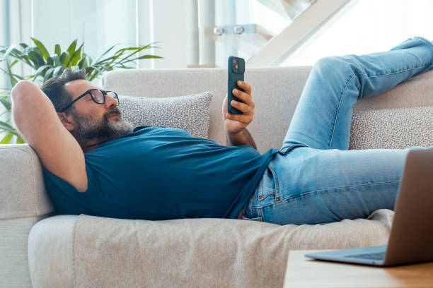 istock One man laying on sofa in chilling relaxation using mobile phone to surf the net or scrolling social media contents. Lazy afternoon people with technology and connection. Enjoying smartphone app male 2154832595