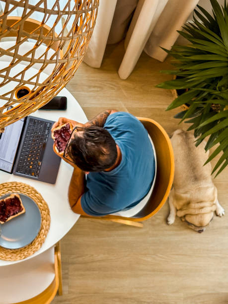istock Vertical above view of man having breakfast time at home alone using laptop at the table. Hotel room or cozy apartment concept modern people lifestyle working early checking emails or notifications 2154833379