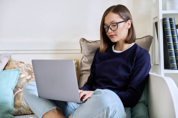 istock Young woman in glasses working at home, sitting on couch using laptop 2154833979