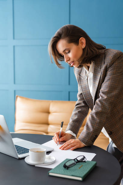istock Beautiful brunette woman standing at desk, holding pen and working with documents. 2154835224
