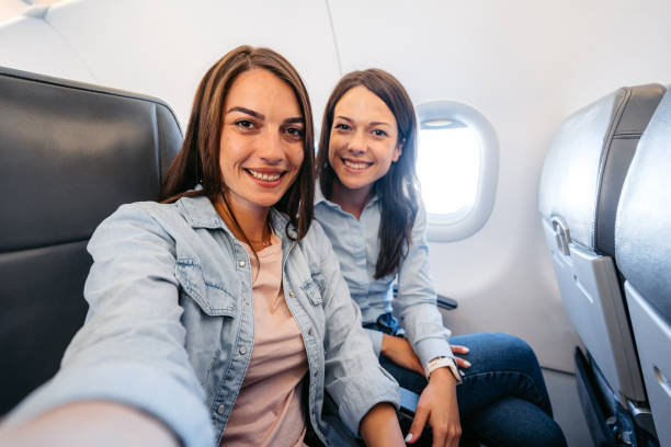 Two Young Female Friends Taking Selfies In An Airplane