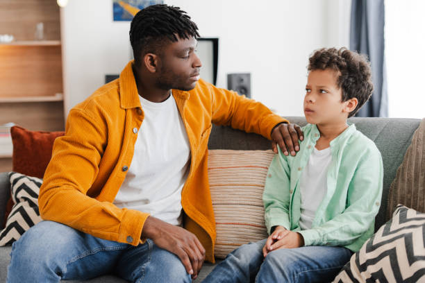 istock Young African American man talking with with little offended son while sitting on comfortable sofa 2154836546