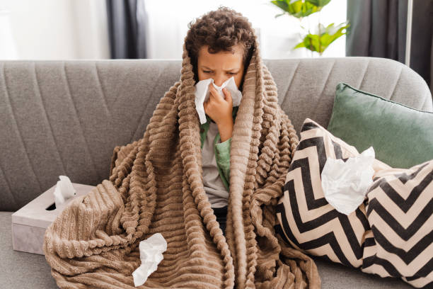 istock Little upset African American boy has a cold, holding napkin, covered with blanket 2154836621