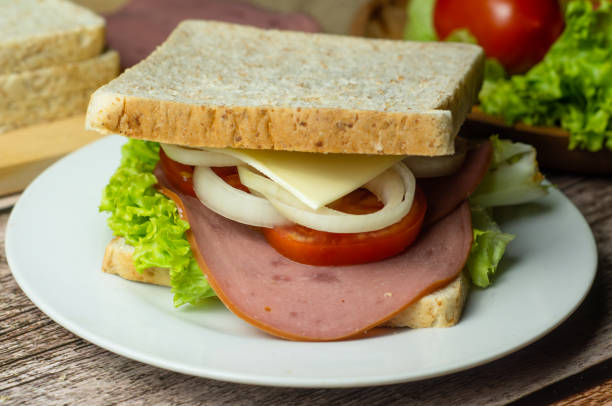 A delicious close-up stock image of a smoked beef sandwich made with wheat bread, fresh lettuce, cheddar cheese, onions, tomatoes, and tender smoked beef. Served on a rustic wooden table, this appetizing shot is perfect for food blogs, restaurant promotions, menu designs, and culinary content. Ideal for showcasing homemade sandwiches, gourmet deli foods, or healthy meal options.