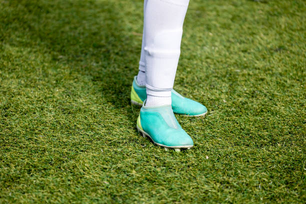 A partial view of a soccer player standing on a grass field with a focus on the legs and soccer cleats