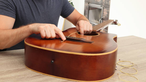 istock Man changing the strings of a guitar at home. Man's hand are installing or replacing strings on a classical guitar. 2154849505
