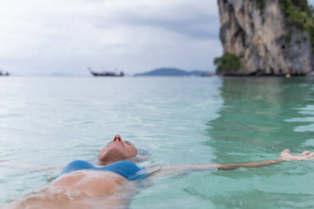 A woman in a blue bikini floats peacefully in clear turquoise waters, with a majestic rocky island in the background.