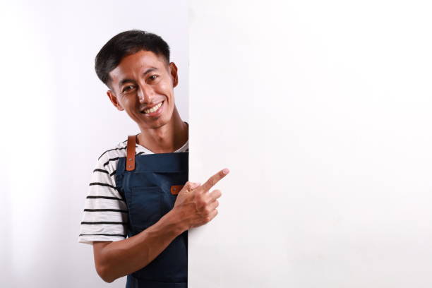istock Happy Asian man in apron pointing something on white advertisement board on white background 2154852759