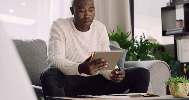 istock Remote work, tablet and black man on sofa for online communication, website and networking. Startup career, working from home and person with digital tech and notes for internet, research and project 2154852965