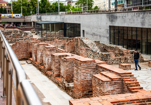 Part of the ruins of the ancient Roman city of Serdica, in the centre of Sofia, Bulgaria. They are on a lower level from the main street, en route to Serdica 2 underground station. A museum containing more excavations is behind the windows on the left. A man is walking through the ruins, and a group of people is looking down from the far end.