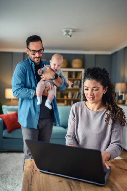 istock Family with a baby at home, mom using a laptop. 2154856659