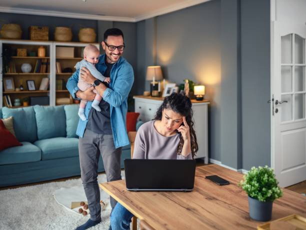 istock Family with a baby at home, mom using a laptop. 2154858493