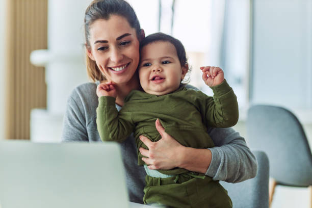 istock A happy mother holding her baby while working on her laptop from home 2154862331