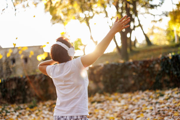 Portrait of mature woman listening to music and dancing in nature on sunny autumn day