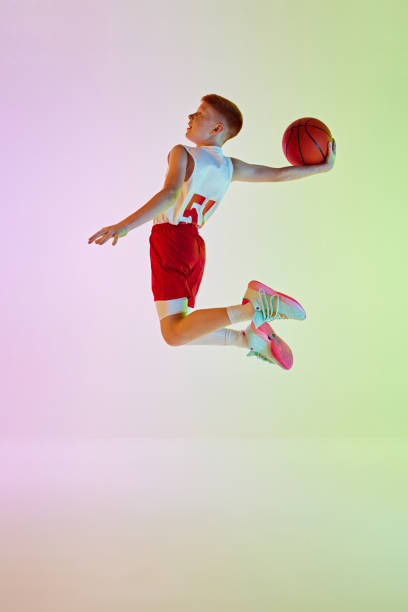 istock Side view full-length image of boy, basketball player during game in motion, practicing, throwing ball against gradient background in neon light 2154879437