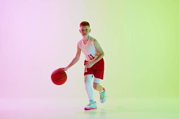 istock Focused boy, basketball player training, playing, dribbling ball against gradient background in neon light 2154879467