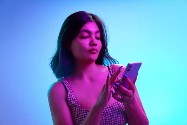 istock Young Indian woman using smartphone, chatting in pink neon light against gradient blue background. Social media concept. 2154884599