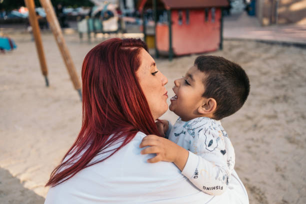 Heartwarming moment as a mother with red hair cuddles her young son at a playground during golden hour