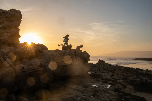 Young woman jumps between stones on beach at sunset