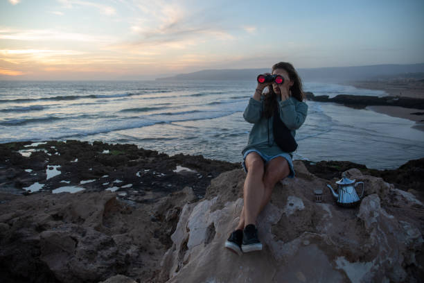istock Young uses binoculars on rocky shoreline 2154911380