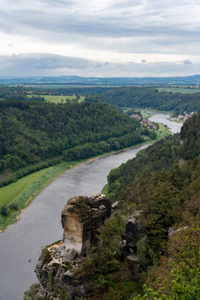 A river flows through a valley with a mountain in the background. The sky is cloudy and the scene is peaceful