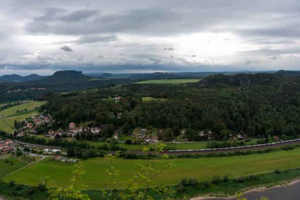 A train is traveling through a lush green countryside. The train is long and has many cars. The sky is cloudy and the landscape is peaceful