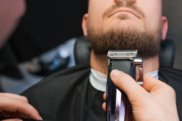Master skillfully trims the clients beard using an automatic trimmer in the barbershop.