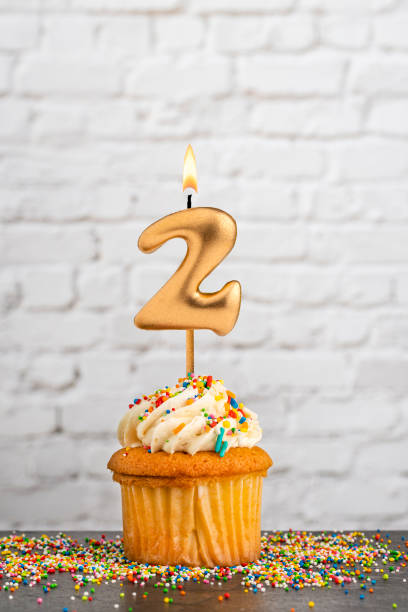 istock Golden birthday candle number 2 with cupcake - White block wall background 2154938111