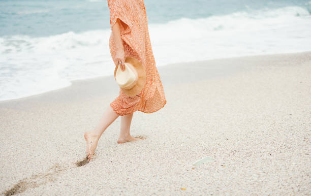 istock Woman Walking on Sandy Beach Holding Hat 2154941546